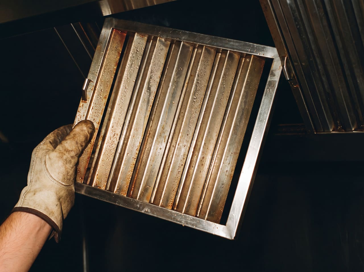 A grease-loaded baffle filter lifted out of a hood filter bank by hand.