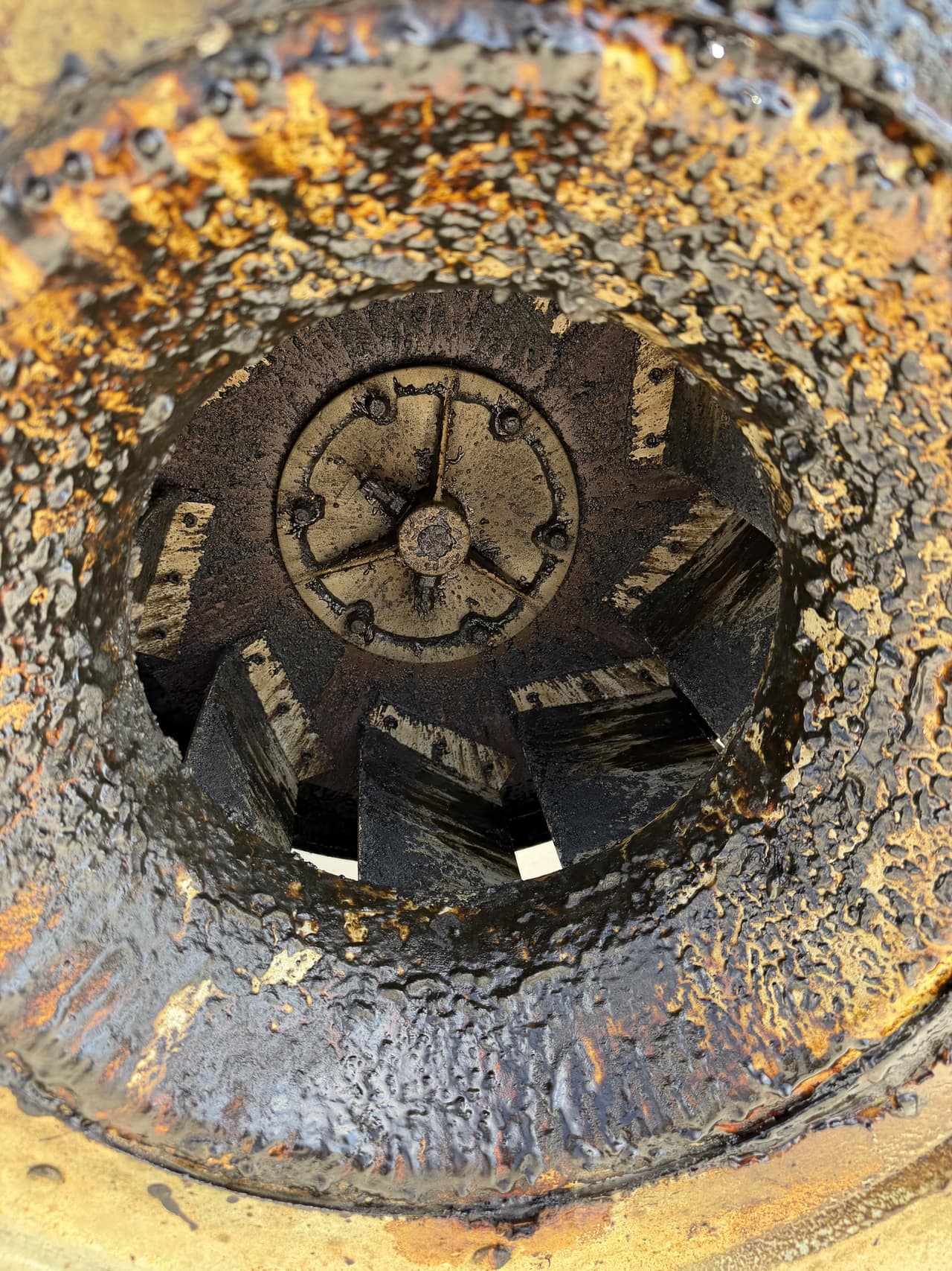 A rooftop exhaust fan housing and fan blades coated with heavy grease buildup before cleaning.
