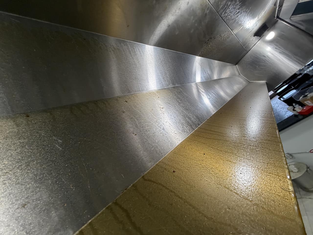 The stainless-steel interior of a restaurant exhaust hood and plenum photographed during cleaning service.