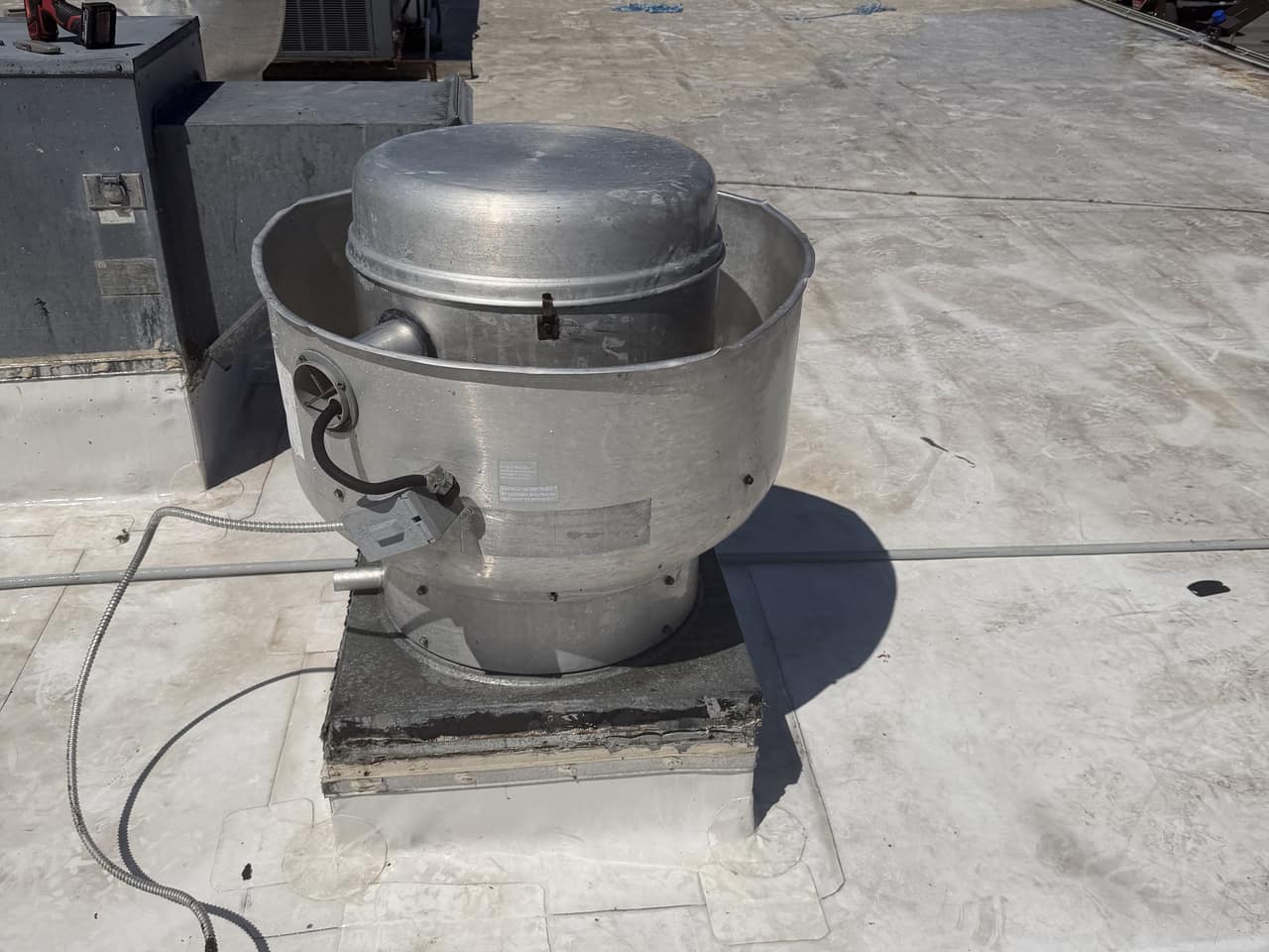 An assembled rooftop exhaust fan with its cleaned metal housing visible on the roof.